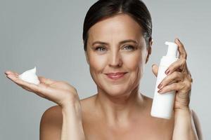 Beautiful middle aged woman holding bottle of cleansing foam or sunscreen lotion photo