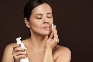 Beautiful middle aged woman with a cotton pad and bottle of cleansing liquid photo