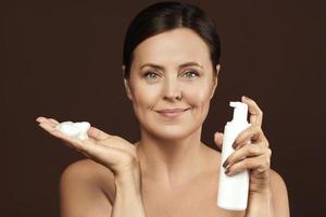 Beautiful middle aged woman holding bottle of cleansing foam or sunscreen lotion photo