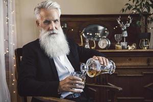 Handsome bearded senior man pouring whiskey into the glass photo