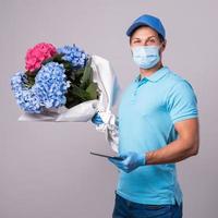 joven repartidor con un ramo de flores lleva guantes y máscara de prevención foto