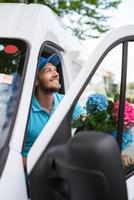 el mensajero dentro de la furgoneta blanca durante la entrega de flores está esperando a un cliente foto