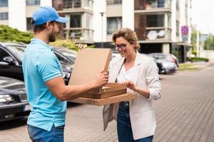 Delivery man wearing blue uniform delivers pizza to a woman client photo