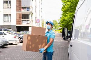 Delivery man wearing prevention mask and gloves is holding stack of the cardboard boxes photo