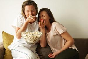 Two beautiful girlfriends watching tv show and eating popcorn photo