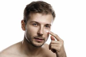 Men's beauty. Young man is applying moisturizing and anti aging cream on his face photo