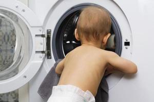 Cute baby boy is looking inside the washing machine photo