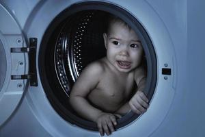 Scared baby boy sitting inside the washing machine photo