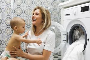 Mother and her little baby son are loading washing machine photo