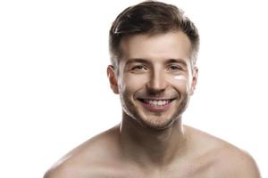 Men's beauty. Young man is applying moisturizing and anti aging cream on his face photo