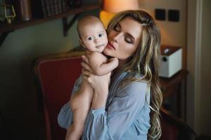 Young beautiful mother wearing luxury grey dress holding her baby on hands photo