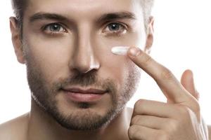 Men's beauty. Young man is applying moisturizing and anti aging cream on his face photo