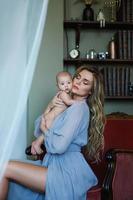 Young beautiful mother wearing luxury grey dress holding her baby on hands photo