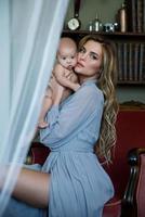 Young beautiful mother wearing luxury grey dress holding her baby on hands photo