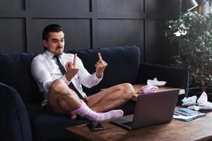 Angry businessman without pants showing rude gesture into the laptop's camera photo