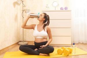 mujer embarazada está bebiendo batido de proteínas después de su entrenamiento de fitness en casa foto