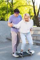 Carefree teenage couple in a skate-park. Guy giving a lesson of skateboarding for his girlfriend. photo