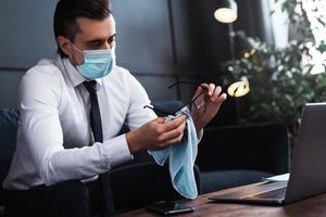 Young businessman wearing prevention mask is cleaning his eyeglasses photo