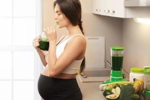 Happy pregnant woman drinking healthy green smoothie photo