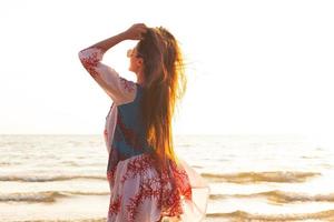 una joven encantadora que lleva un vestido hermoso camina por la orilla del mar foto