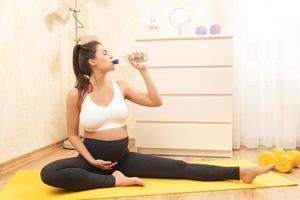 Pregnant woman with a bottle of fresh water during her fitness workout at home photo