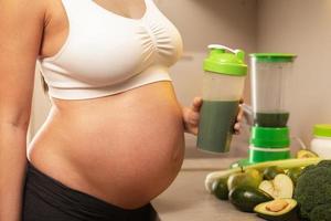 Pregnant woman holding shaker with a green protein cocktail photo