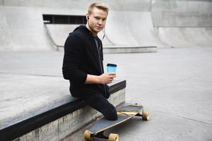 Handicapped guy with a cup of coffee before longboard riding in a skatepark photo