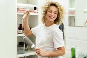 Young happy woman using hairdryer after for her curly hair photo