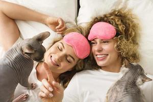 Two beautiful girls lying in a bed with a cats photo