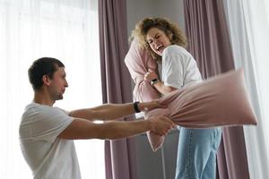 pareja feliz durante la pelea de almohadas en su apartamento foto