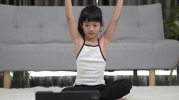 toma en cámara lenta, niña asiática sentada en una alfombra entrenando con una tableta en pose de meditación en casa video