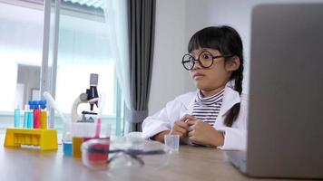 grappig meisje in brillen lachen met gelukkig, laptopcomputer en apparaat om te experimenteren met vloeistoffen op tafel, terwijl ze wetenschapschemie studeert, selectieve focus