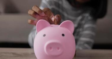 closeup da menina mão colocando moedas no cofrinho enquanto está sentado no chão na sala de estar. financeiro, economizando dinheiro e conceito de investimento. video