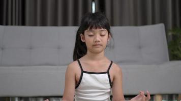 alejar la toma, niña asiática sentada en la alfombra y colocar la mano en la rodilla abre los ojos después de una pose de meditación en casa