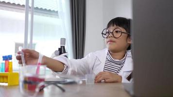 grappig meisje in bril glimlach met Vrolijk, gebruik microscoop, laptop computer en apparaat van experimenteren met vloeistoffen Aan tafel, terwijl aan het studeren wetenschap chemie, selectief focus video