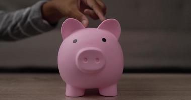 Closeup of Two hand girls putting coins into piggy bank while sitting on floor in living room. Front view piggy bank on table. Financial, saving money and investment concept. video