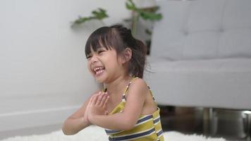 niña asiática graciosa sentada en la alfombra en pose de meditación en casa, cerró los ojos y se rió cuando abrió los ojos