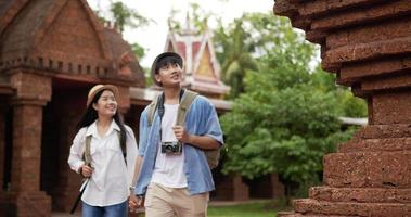 Happy asian traveler couple with hat hand together while visiting at ancient temple. Smiling young man and woman walking and looking ancient temple. Holiday, travel and hobby concept. video