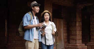 Portrait of Happy Asian couple checks location on smartphone online map in ancient temple. Smiling male and female using mobile phone navigating map application. Holiday, travel and hobby concept. video