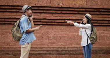 Happy Asian traveler couple meet up at ancient temple. Smiling young man and woman talking on smartphone and waving hand. Dating and holiday concept. video