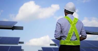 Handheld shot, Close up portrait of young engineer man in protective helmet. standing crossed arms, looking at camera and smiles in solar farm video