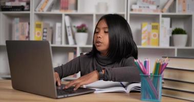 retrato en la cabeza de una niña asiática sonriente con auriculares hablando y agitando la mano a través de una computadora portátil mientras se sienta en el escritorio en casa. mujer joven que estudia en línea a través de una computadora portátil y conferencias, discutiendo con el maestro. video