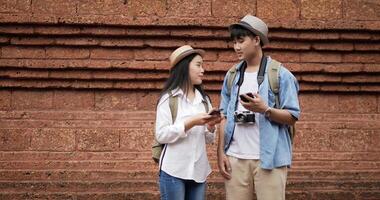 Portrait of Happy Asian couple checks location on smartphone online map in ancient temple. Smiling male and female using mobile phone navigating map application. Holiday, travel and hobby concept. video