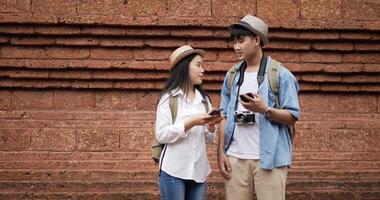 Portrait of Happy Asian couple checks location on smartphone online map in ancient temple. Smiling male and female using mobile phone navigating map application. Holiday, travel and hobby concept. video