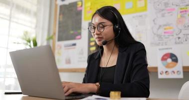 el primer plano de unas gafas femeninas felices usa videollamadas con auriculares en una computadora portátil. conferenciante de seminario web de empresaria que transmite capacitación web en vivo. agente del centro de llamadas, gerente de soporte de servicio hablando con el cliente. video