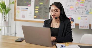 Seitenansicht der glücklichen weiblichen Brille trägt Headset-Videoanrufe auf dem Laptop. Webinar-Sprecherin für Geschäftsfrau, die Live-Web-Schulungen streamt. Call-Center-Agent, Service-Support-Manager, der mit dem Kunden spricht. video