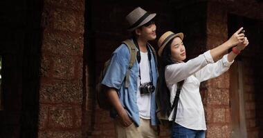 gelukkig Aziatisch paar selfie Aan smartphone in oude tempel. jong vrouw Holding mobiel telefoon. mannetje en vrouw glimlachen en op zoek Bij mobiele telefoon. vakantie, reizen en hobby concept. video