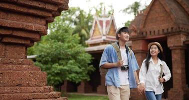 heureux couple de voyageurs asiatiques avec chapeau main ensemble lors d'une visite à l'ancien temple. souriant jeune homme et femme marchant et regardant l'ancien temple. concept de vacances, de voyage et de passe-temps. video