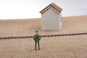 Man figurine and a Model house beyond the chain photo