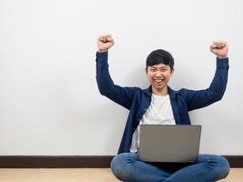 Man with laptop sit on floor feeling happy show fist up white background photo